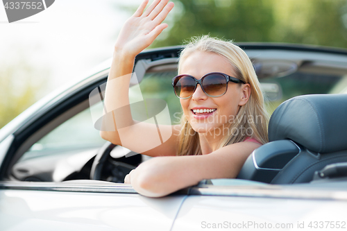 Image of happy young woman in convertible car waving hand