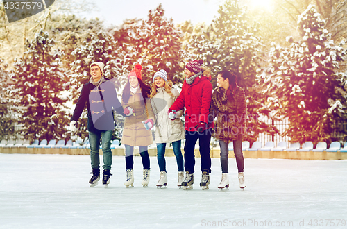 Image of happy friends ice skating on rink outdoors