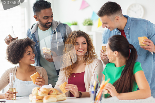 Image of happy friends or team eating at office party