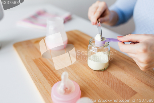 Image of hands with jar and scoop making formula milk