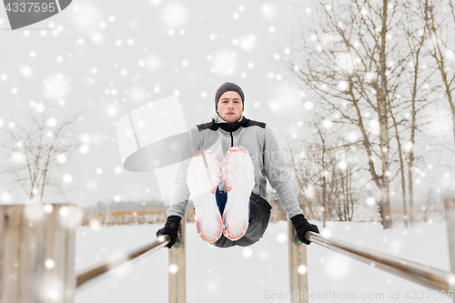 Image of young man exercising on parallel bars in winter