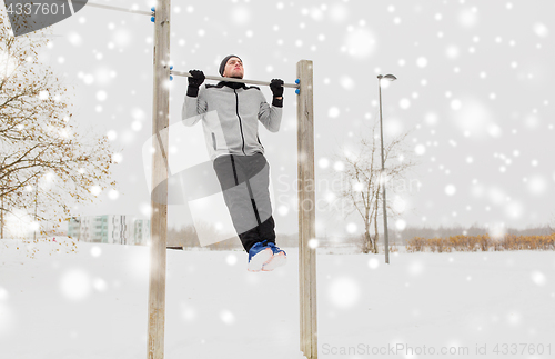 Image of young man exercising on horizontal bar in winter