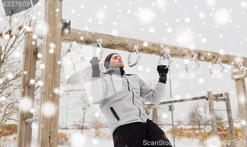 Image of young man exercising on horizontal bar in winter