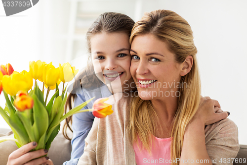 Image of happy girl giving flowers to mother at home