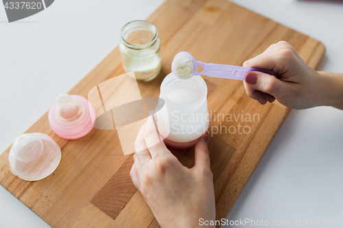 Image of hands with bottle and scoop making formula milk