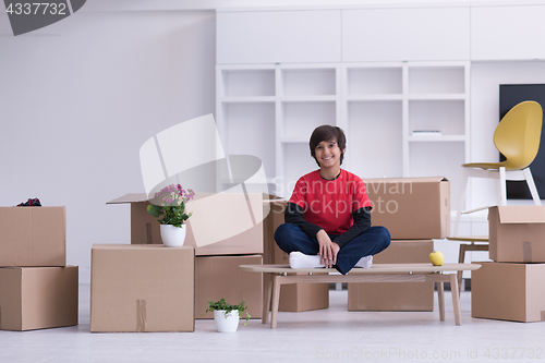 Image of boy sitting on the table with cardboard boxes around him