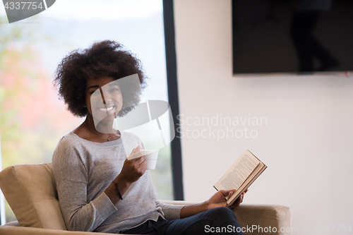 Image of black woman reading book  in front of fireplace