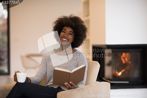 Image of black woman reading book  in front of fireplace