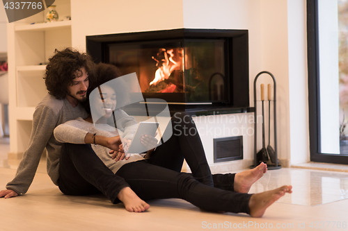 Image of multiethnic couple using tablet computer on the floor