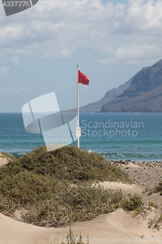 Image of The red flag weighs in the wind at Surfers Beach Famara on Lanza