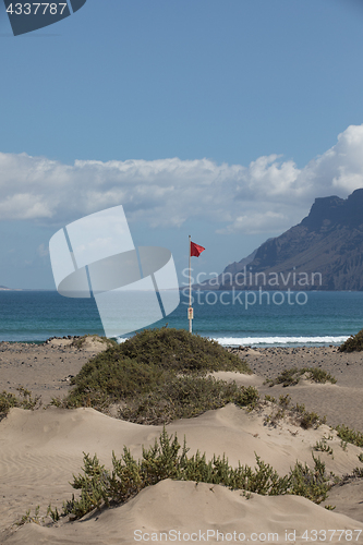 Image of The red flag weighs in the wind at Surfers Beach Famara on Lanza