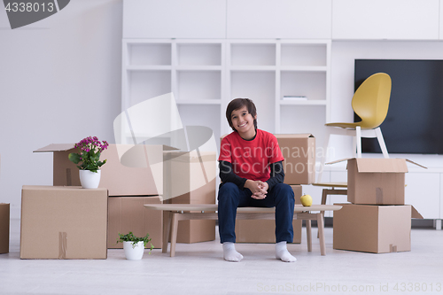 Image of boy sitting on the table with cardboard boxes around him