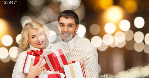 Image of happy couple in sweaters holding christmas gifts