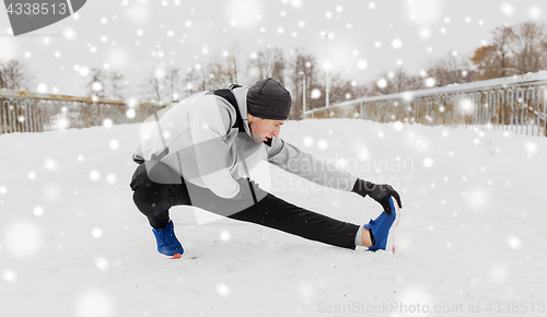 Image of man exercising and stretching leg on winter bridge