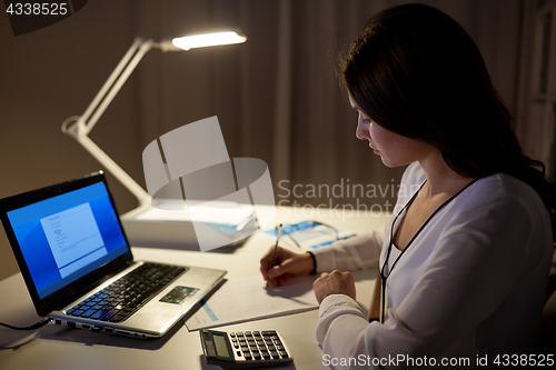 Image of woman with calculator and papers at night office