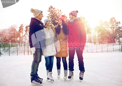 Image of happy friends ice skating on rink outdoors