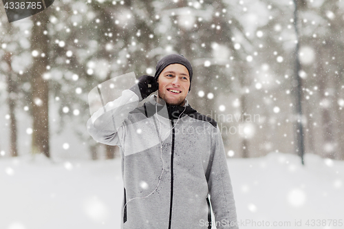 Image of happy sports man with earphones in winter forest