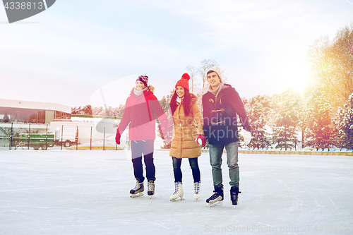 Image of happy friends ice skating on rink outdoors