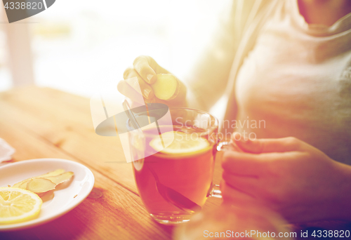 Image of close up of woman adding ginger to tea with lemon