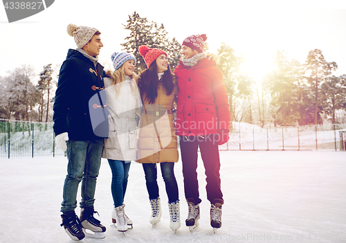 Image of happy friends ice skating on rink outdoors