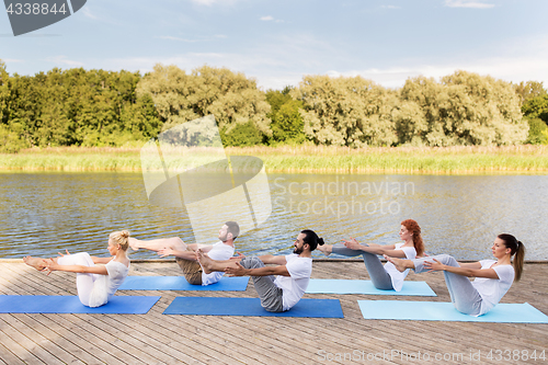 Image of people making yoga in half-boat pose outdoors