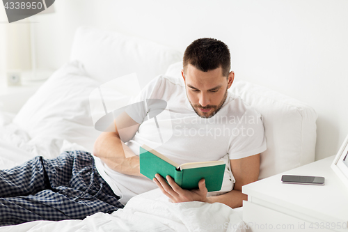 Image of man reading book in bed at home