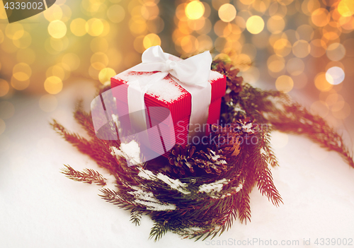 Image of christmas gift and fir wreath with cones on snow