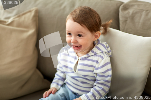 Image of happy smiling baby girl sitting on sofa at home