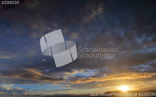 Image of Sun setting sunburst behind mountain with blue sky and clouds ti