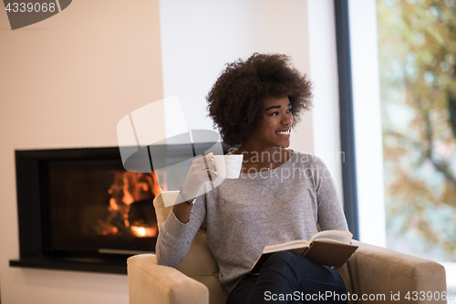 Image of black woman reading book  in front of fireplace