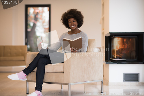 Image of black woman reading book  in front of fireplace