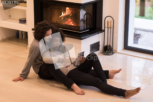 Image of multiethnic couple using tablet computer on the floor