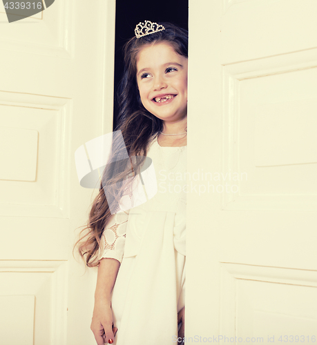 Image of little cute girl at home, opening door well-dressed in white dre