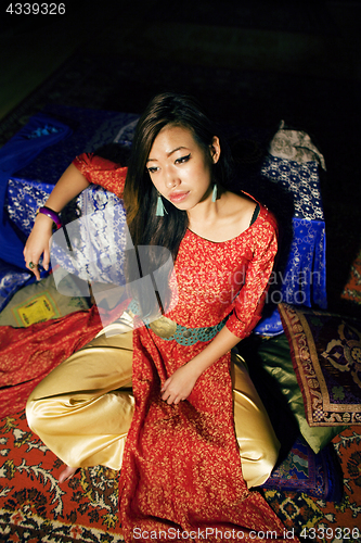 Image of young pretty asian girl in bright colored interior on carpet