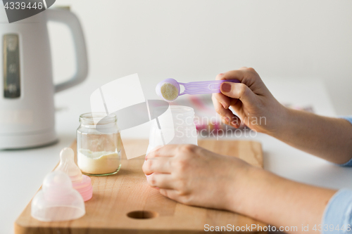 Image of hands with bottle and scoop making formula milk