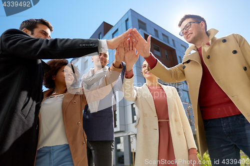 Image of group of happy people making high five in city