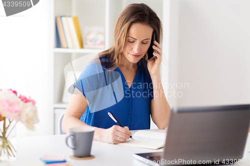 Image of woman with notepad calling on smartphone at office