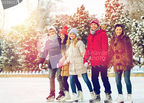 Image of happy friends ice skating on rink outdoors