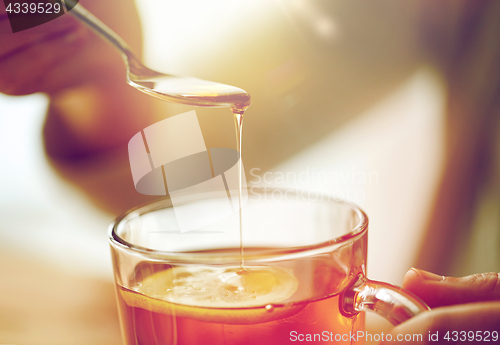 Image of close up of woman adding honey to tea with lemon