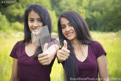 Image of Portrait of a happy sisters twins showing thumbs up 