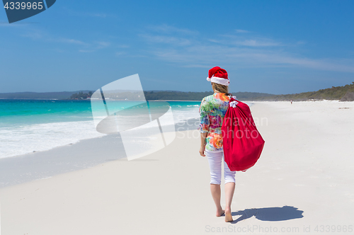 Image of Christmas in Australia - woman walking along beach with festive 