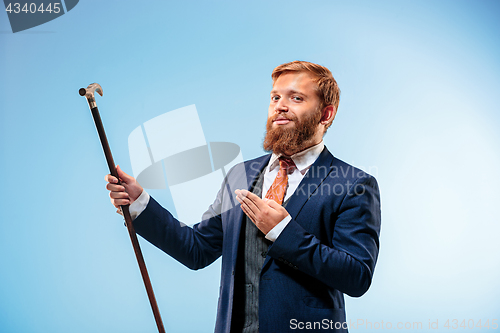 Image of Tattooed bearded man in a suit holding cane.