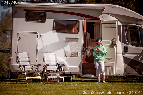 Image of Woman is standing with a mug of coffee near the camper RV.