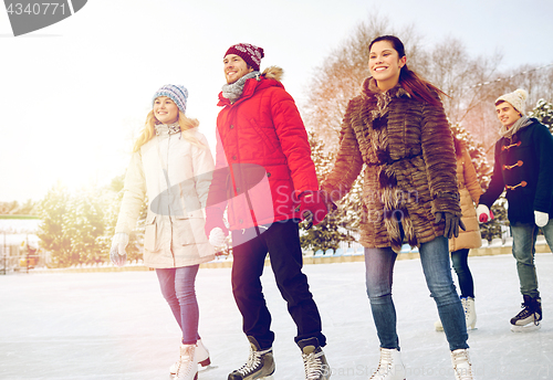 Image of happy friends ice skating on rink outdoors