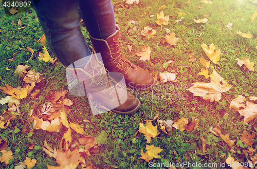 Image of female feet in boots and autumn leaves on grass