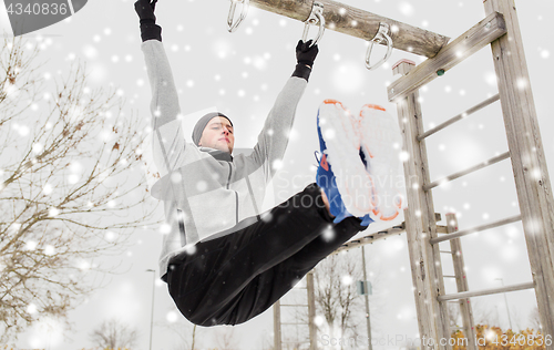 Image of young man exercising on horizontal bar in winter