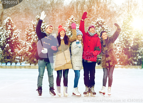 Image of happy friends ice skating on rink outdoors