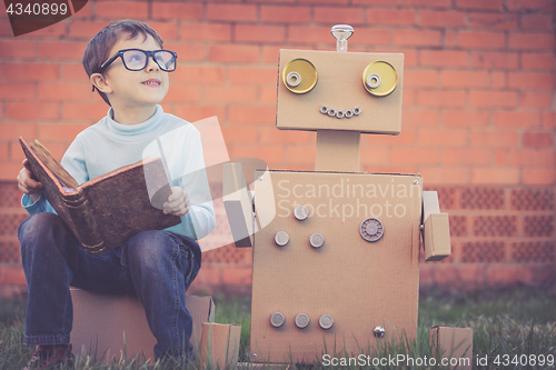 Image of One little boy reading to  robot from cardboard boxes outdoors. 