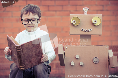 Image of One little boy reading to  robot from cardboard boxes outdoors.