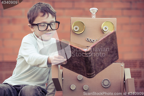 Image of One little boy reading to  robot from cardboard boxes outdoors.